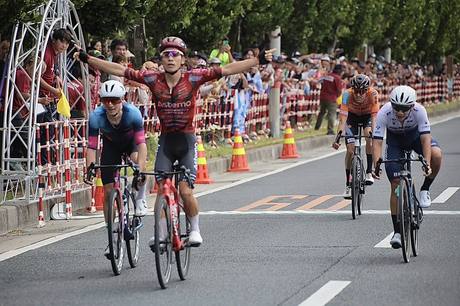 Atsushi Oka remporte le Tour de Okinawa 2025 en levant les bras sur la ligne d’arrivée devant un groupe de poursuivants.