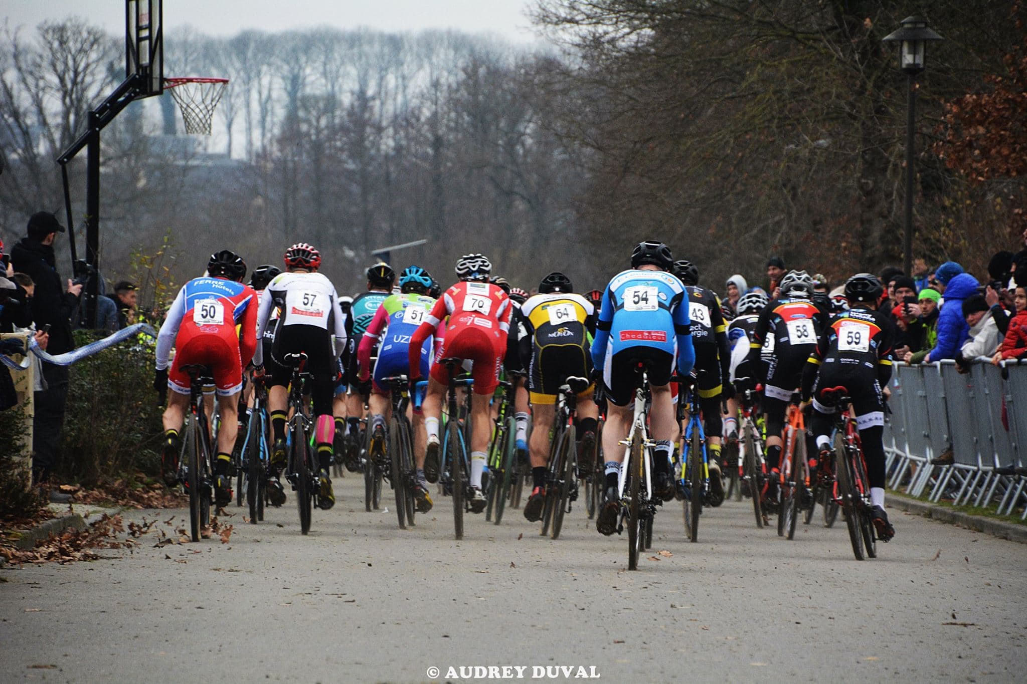 Peloton de cyclistes de dos en pleine course de cyclo-cross sur terrain boueux
